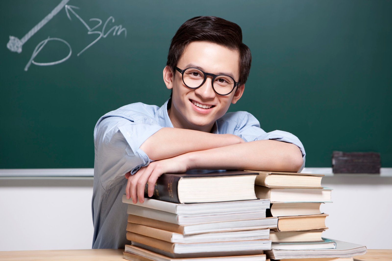 Happy male Chinese teacher with textbooks in classroom